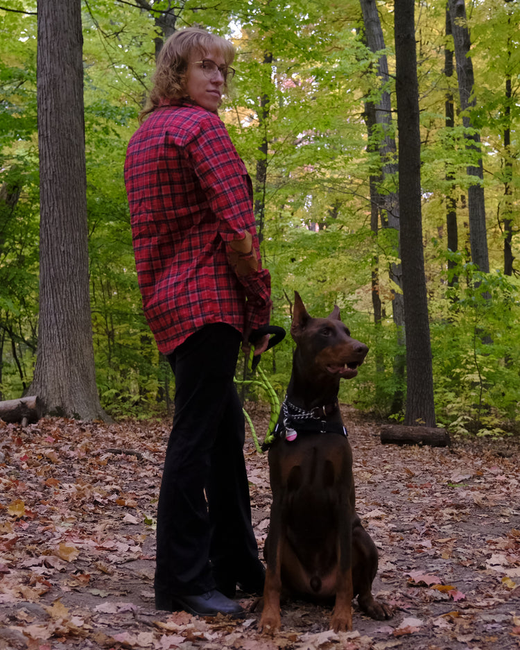 Person in a red plaid shirt standing with a dog in a forest